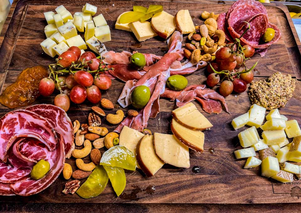 Charcuterie Board with assorted cheeses, meats, pickled vegetables, nuts, jams, spreads, crostini, and grapes.