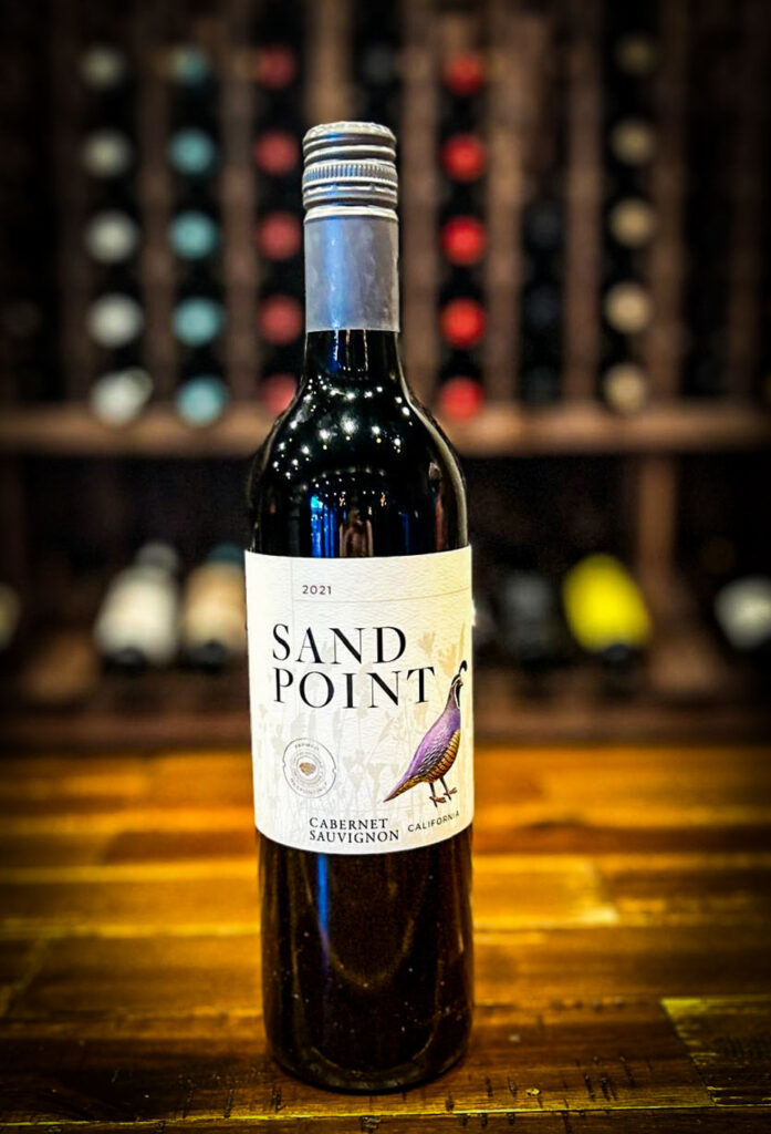 Bottle of Sand Point Organic Wine with a glass showcasing its bold dark cherry and ripe raspberry flavors