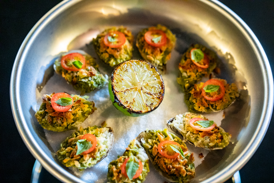 Pesto Rockefeller Oysters topped with basil pesto, Parmesan, cherry tomatoes, and crispy panko, served on a bed of rock salt at Simone on Sunset.