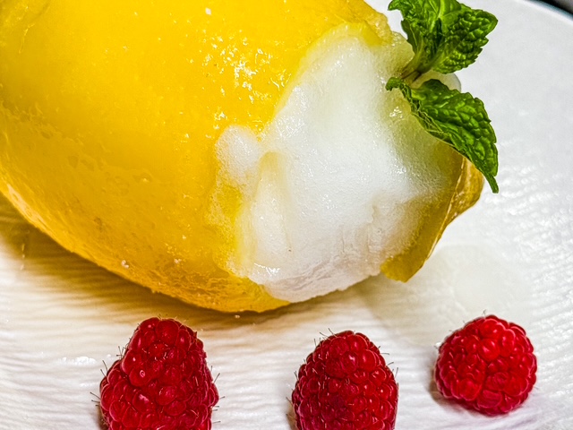 A whole Sicilian lemon hollowed out and filled with creamy, tangy lemon sorbet, served as a refreshing dessert.