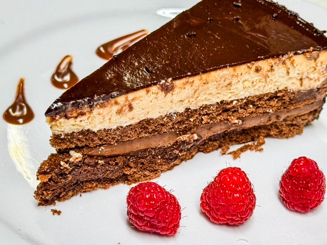 A slice of rich chocolate temptation cake with a glossy chocolate ganache, hazelnut pastry cream filling, and a smooth chocolate glaze on top.